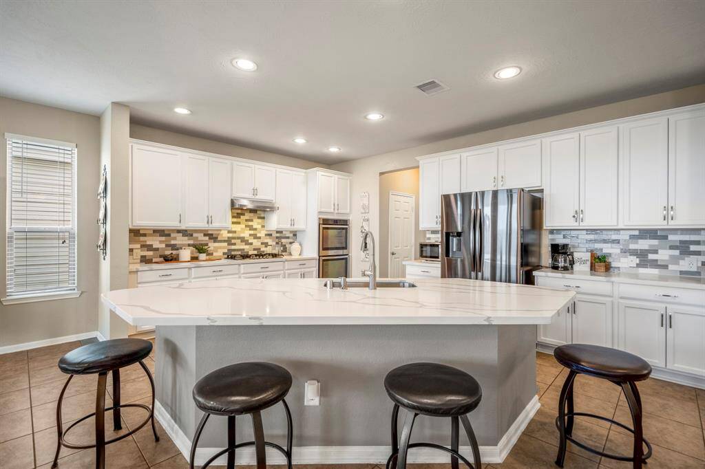This modern kitchen features a spacious island with seating, stainless steel appliances, and ample white cabinetry. The backsplash adds a stylish touch, while recessed lighting brightens the space. Ideal for cooking and entertaining.