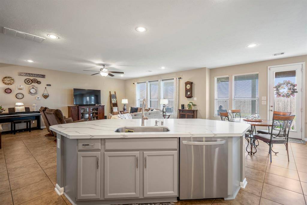 This photo showcases an open-concept living area with a modern kitchen island featuring a sink and dishwasher. The room is bright and spacious, with ample natural light from large windows and a glass door leading outside.