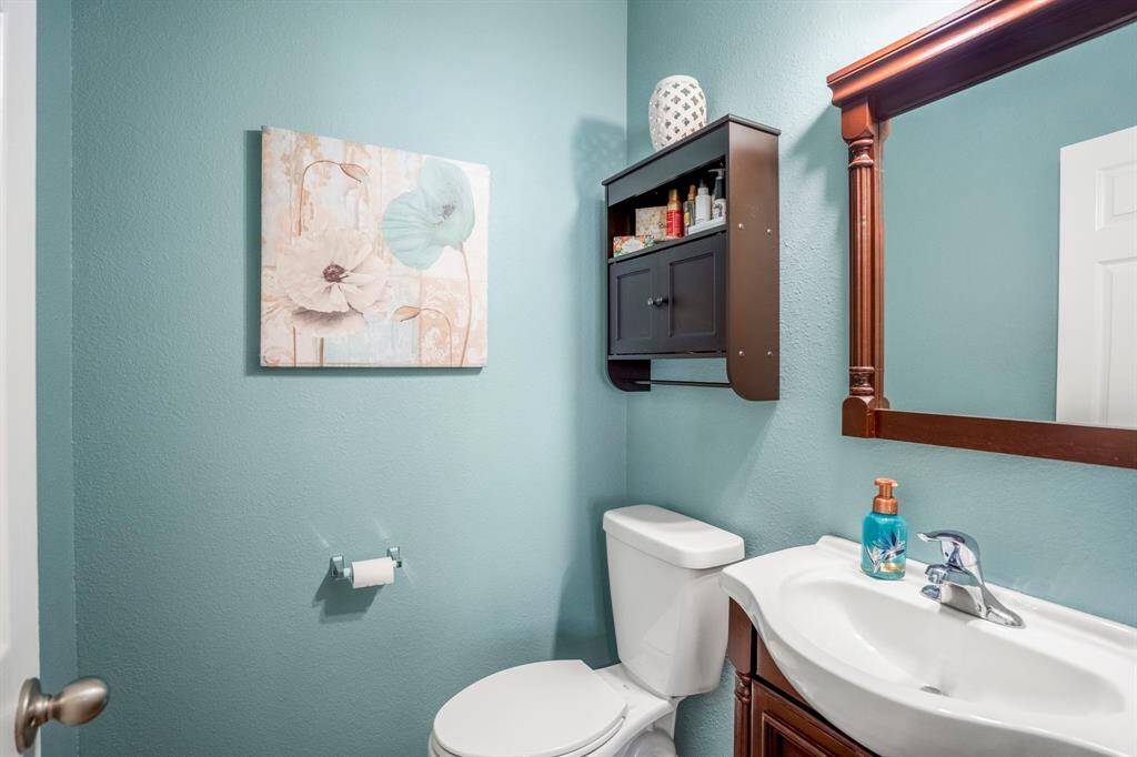This stylish powder bathroom featuring a teal wall, a modern sink with a wooden-framed mirror and a wall-mounted cabinet for storage.