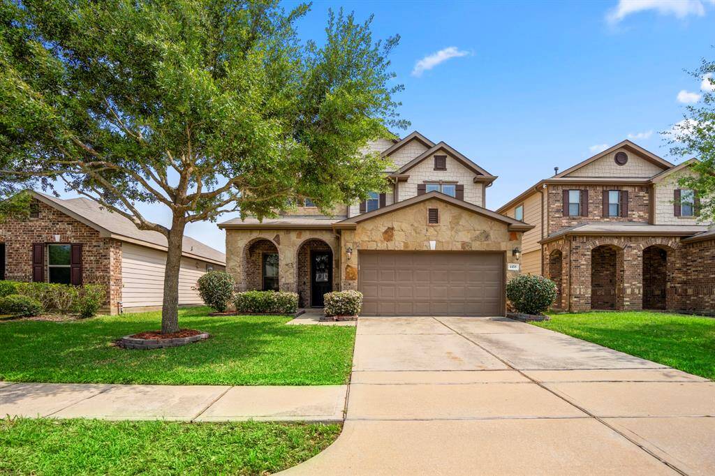 This is a charming two-story home with a stone and brick facade, featuring a two-car garage and a well-maintained front yard with a mature tree. It's situated in a suburban neighborhood with similar style homes.