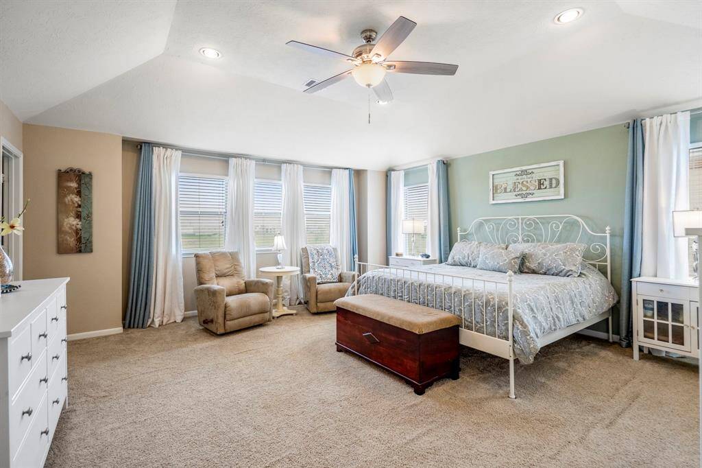 Spacious primary bedroom with plush carpeting, neutral walls, and a ceiling fan.