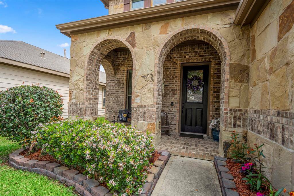 Charming entrance with a stone and brick facade, featuring elegant arches. The well-maintained garden and path lead to a welcoming black front door adorned with a wreath.