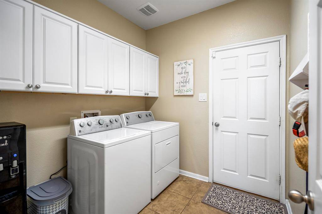 This laundry room features ample white cabinetry for storage. A door provides access to the garage, and the space is well-lit with a neutral color palette.