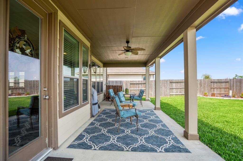 Spacious covered patio with a ceiling fan. It overlooks a well-maintained fenced backyard, perfect for relaxation or entertaining.