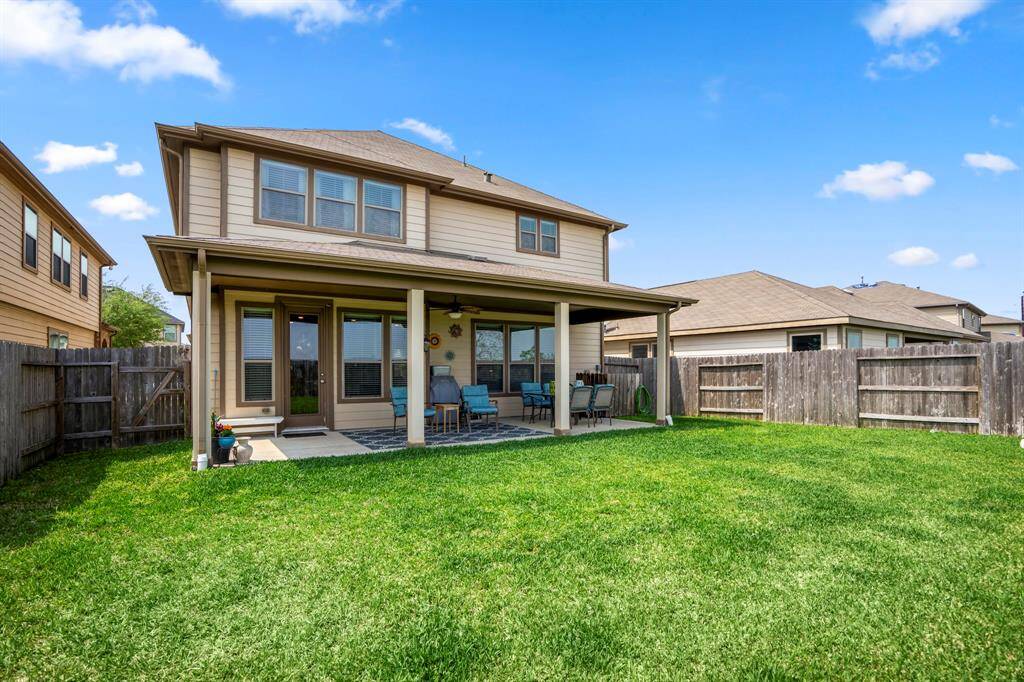 This photo showcases a two-story home with a spacious, fenced backyard. There's a covered patio area with outdoor furniture, ideal for relaxation or entertaining. The lawn is well-maintained, and the property is surrounded by neighboring homes.