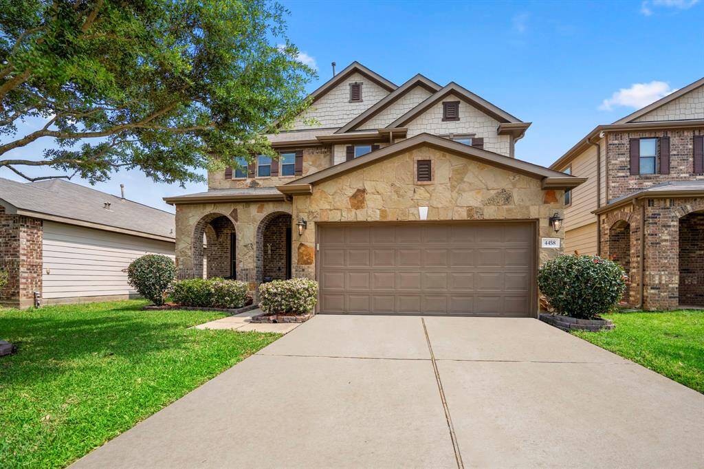 This charming two-story home features a stone and brick facade, a double garage, and a welcoming front porch with arches. It is situated on a neatly landscaped lot with a well-maintained lawn, providing great curb appeal.