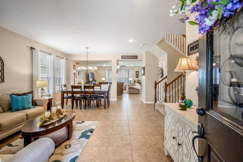This inviting home features an open-concept living and dining area with modern tile flooring, neutral walls, and ample natural light. The space includes a cozy seating area, elegant dining table, and a charming staircase leading to the upper floor. Perfect for comfortable living and entertaining.