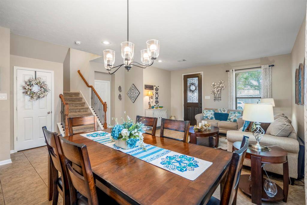 The photo showcases a cozy, open-concept living and dining area. Natural light fills the space, highlighting the neutral tones and elegant lighting fixtures. A staircase leads to the upper level.
