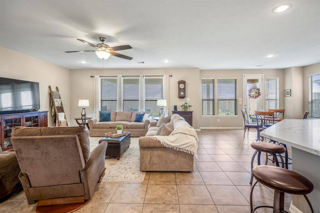 Spacious open-concept living area with tiled floors, neutral colors, and ample natural light. Features cozy seating, a ceiling fan, and a dining area by a large window. Perfect for entertaining and family gatherings.