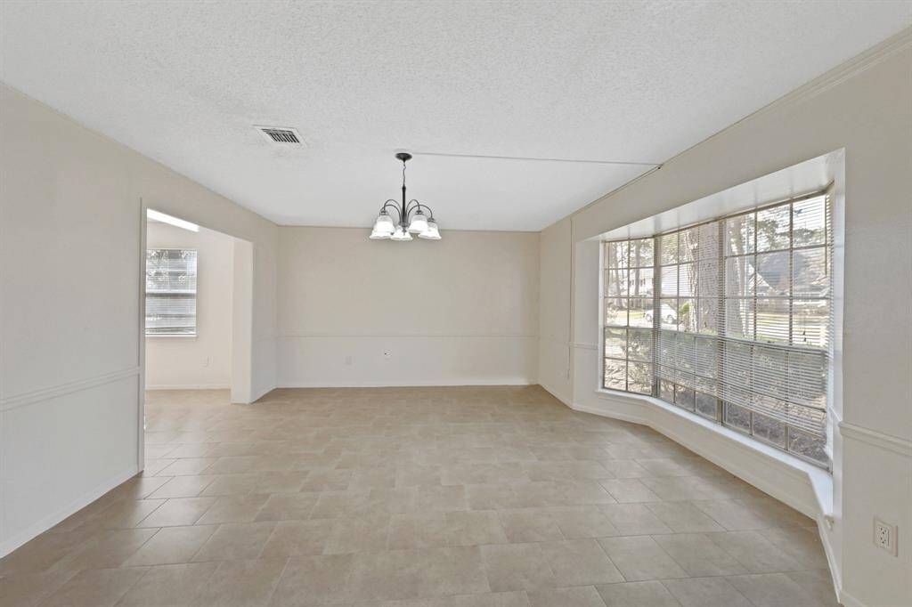 Beautiful bright, spacious dining area with neutral walls and tiled flooring. It features a large bay window allowing ample natural light and a modern overhead light fixture.
