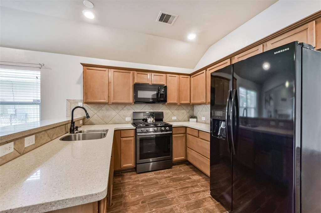 Open kitchen with black and stainless-steel Samsung kitchen appliances and granite counter tops and a tile back splash for easy cleaning. Refrigerator stays with the home.