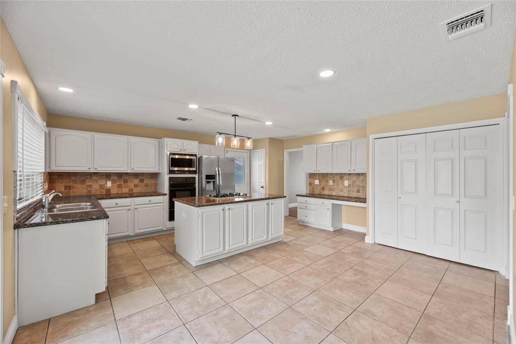 Gorgeous island kitchen with white cabinetry, tile backsplash, gas cooktop and a built-in desk.