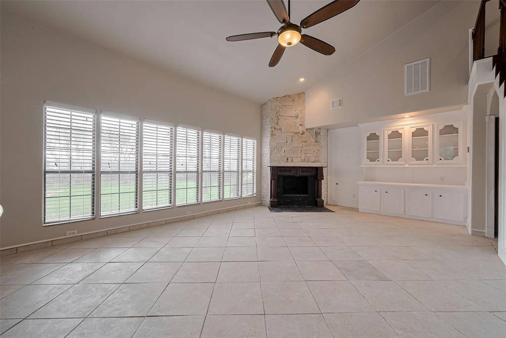 The spacious main living area boasts soaring ceilings, a dramatic wall of windows overlooking the backyard, and a statement stone fireplace. Built-in cabinetry adds character and storage, making this room the heart of the home.