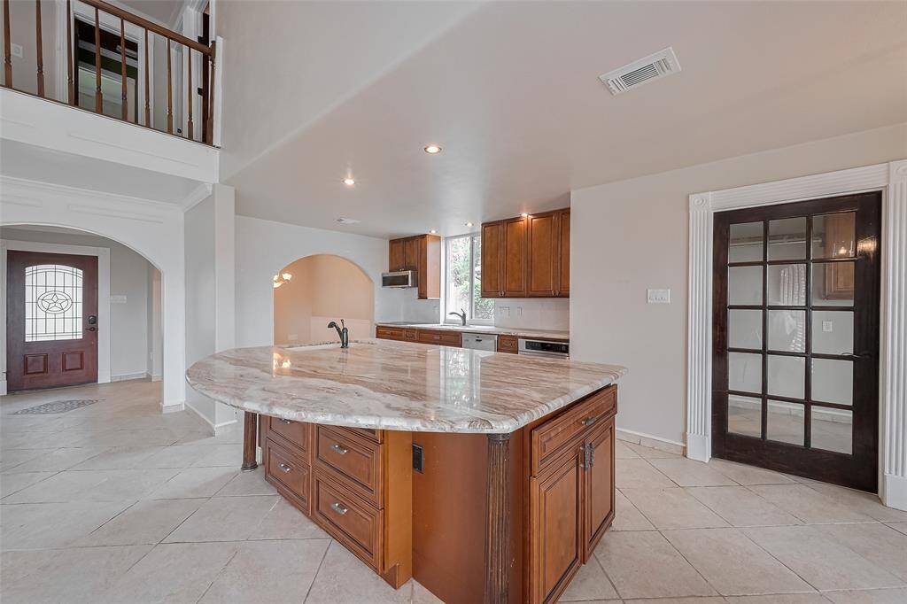 A wide-open kitchen layout offers clear views to the living room and front entry. Arched transitions and warm wood cabinetry complement the sophisticated marble countertops, while the glass-paneled pantry door adds a touch of charm.