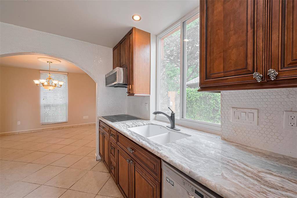 A large picture window over the sink fills the kitchen with sunlight and provides a view of the side yard. Custom cabinetry, penny tile backsplash, and updated fixtures make this a stylish and functional prep area. Wall from kitchen into dining room is all accented with tile.