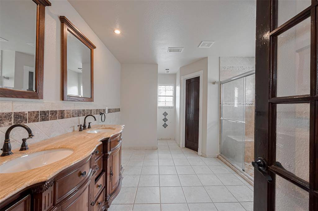 The luxurious primary bathroom features double vanities with elegant granite countertops, framed mirrors, and classic oil-rubbed bronze fixtures. Tile accents and warm wood cabinetry elevate the overall design.