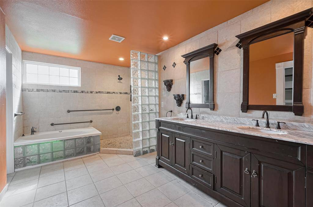 A show-stopping second bathroom featuring a deep soaking tub with glass block accents, a walk-in shower with pebble floor, and bold design choices including a vibrant ceiling and striking dark wood vanity.