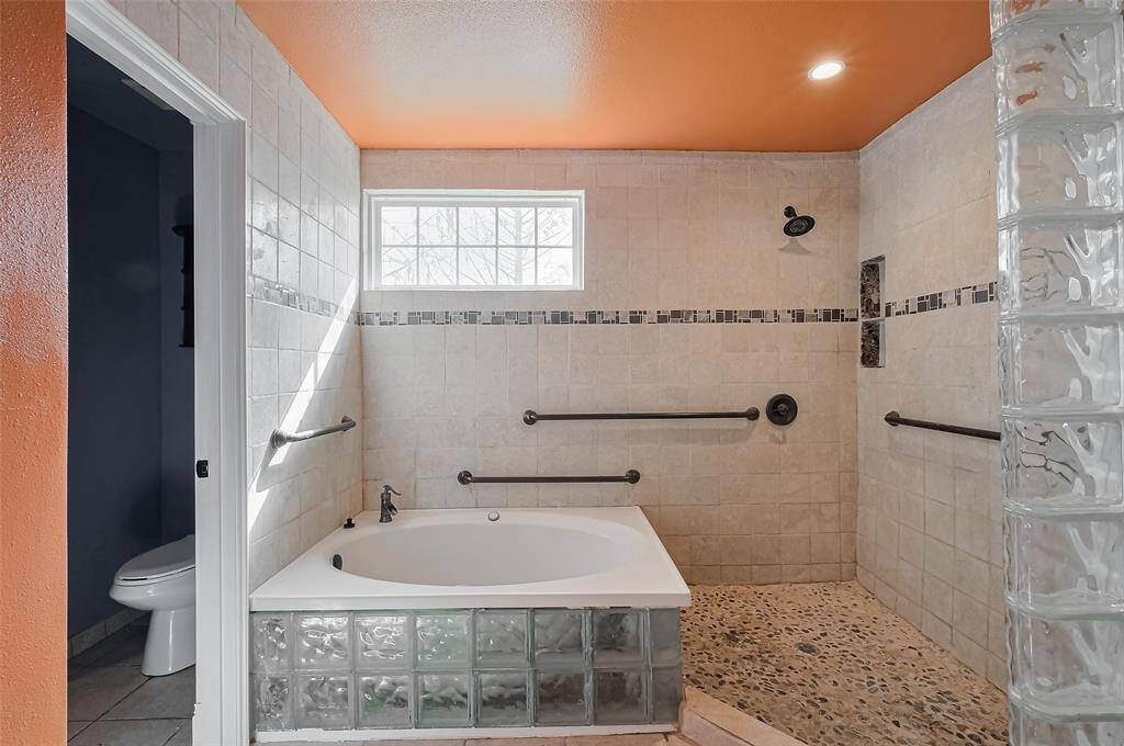 Perfect for relaxation, this bath offers a spa-like atmosphere with a soaking tub surrounded by frosted glass block, paired with a spacious walk-in shower and modern tilework.