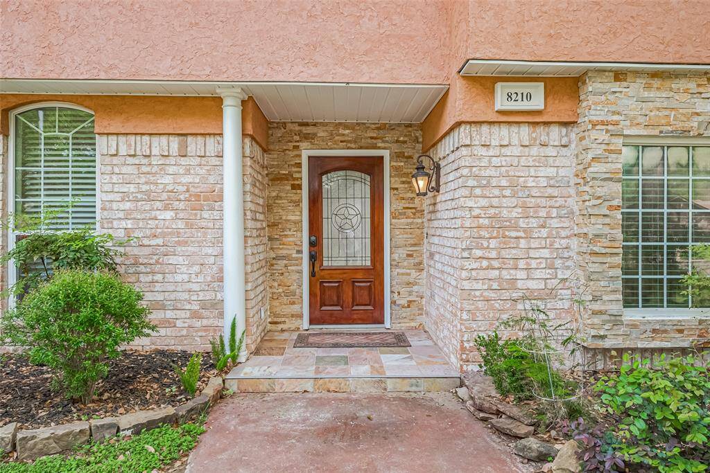 The inviting front porch features stacked stone, tile flooring, and a gorgeous wood door with decorative glass inlay. A classic lantern-style sconce sets the tone for the warmth and character found throughout the home.