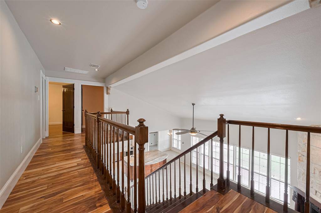 A bird’s-eye view from the upstairs landing highlights the two-story living area, showcasing wood-look floors and iron-spindled railing that adds classic architectural interest.
