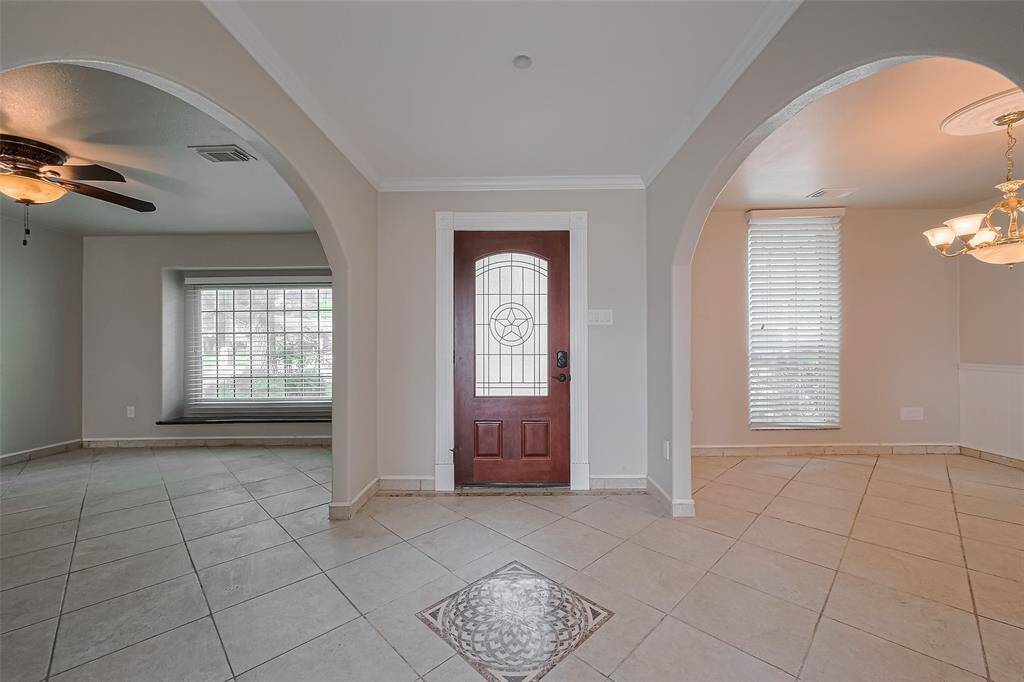 Step into a welcoming foyer that showcases elegant archways, neutral tile flooring, and a rich wood front door with decorative tile inlay. Crown molding and natural light set the tone for the home’s warm, inviting aesthetic.