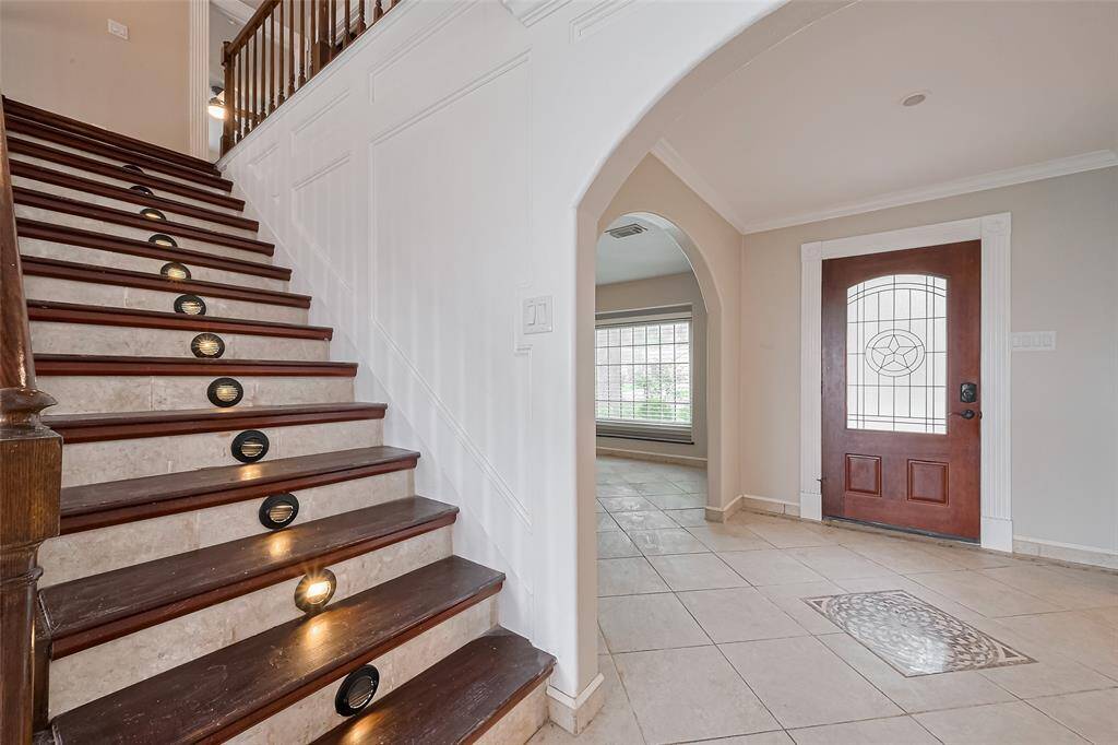 This beautifully detailed staircase features dark wood steps accented by stone tile risers and built-in step lighting—creating both safety and style. Wainscoting and classic trimwork complete the elegant entryway.