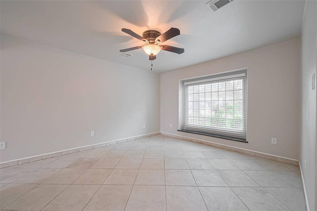 A cozy sitting area just off the entryway features a large front-facing window with deep ledge seating, perfect for relaxing with a view. Neutral tile floors and a ceiling fan make this space versatile for a study, reading nook, or playroom.