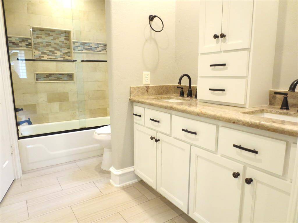 This bathroom features a modern design with a dual-sink vanity, granite countertops, and ample storage. The elegant tiled shower includes a glass door and decorative mosaic accents.