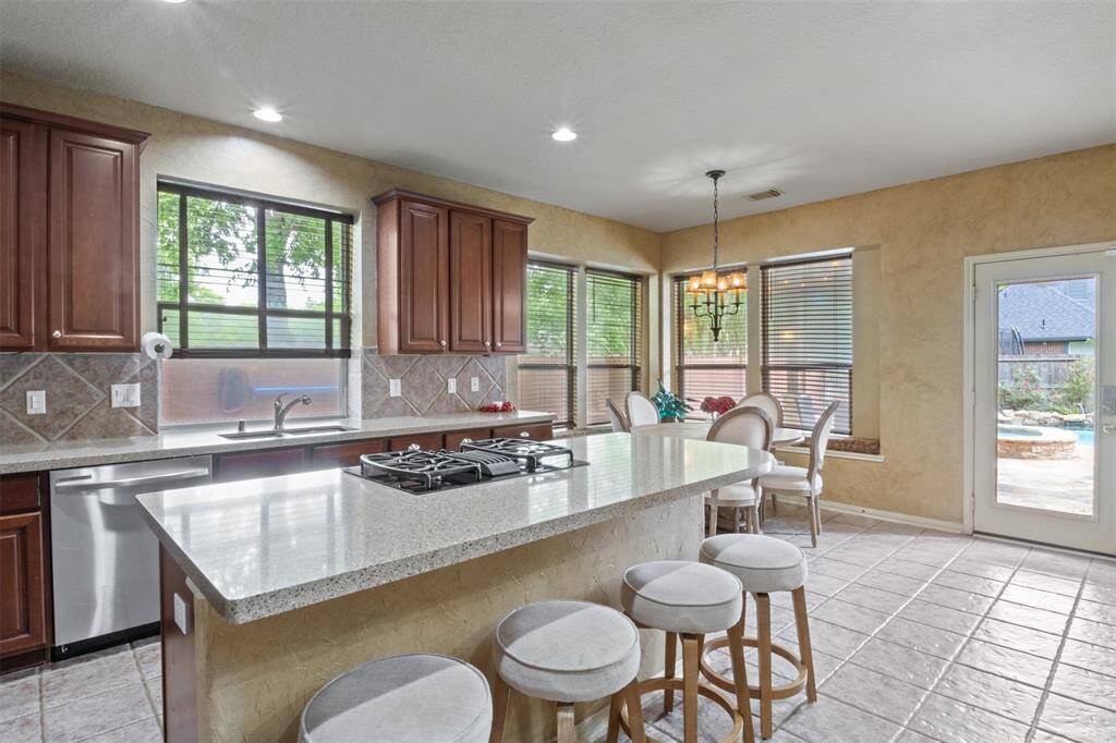 The heart of the home, this sunlit kitchen features an oversized island with gas cooktop, sleek stone counters, and custom cabinetry—perfect for casual mornings or lively evenings of entertaining. Wall-to-wall windows and direct patio access seamlessly blend indoor comfort with outdoor living.