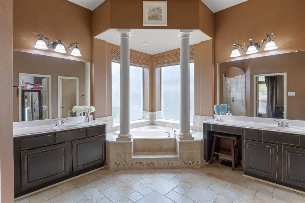 Centered around a deep soaking tub with elegant column accents and panoramic privacy windows, the primary bath offers dual vanities and a layout that feels both grand and serene. A perfect escape to unwind in timeless style.
