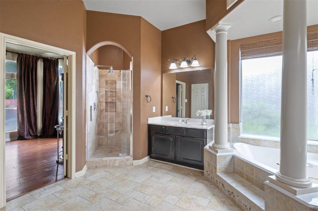 Unwind in the spa-inspired primary bath featuring a glass-enclosed walk-in shower, soaking tub framed by dramatic columns, and dual vanities with generous counter space. Elegant finishes and abundant natural light elevate this space into a daily retreat.
