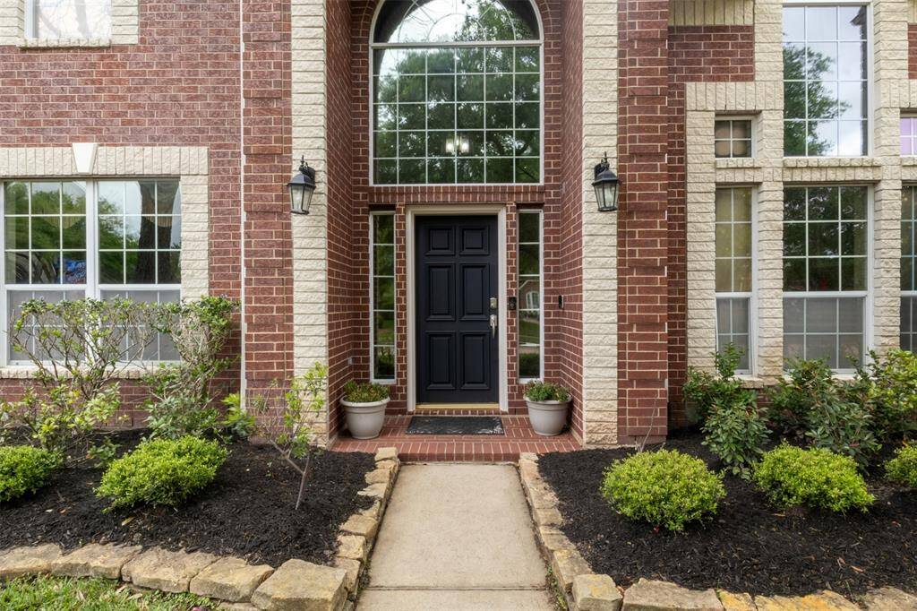 A bold, elegant front door framed by stately brickwork and expansive transom windows sets the tone for a home filled with character and light. Meticulously landscaped beds and a charming brick porch create a lasting first impression.