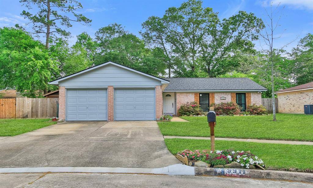 Charming single-story home with a two-car garage, brick exterior, and a well-maintained lawn. The property features a neat driveway and a small garden near the entrance, surrounded by lush greenery and mature trees.