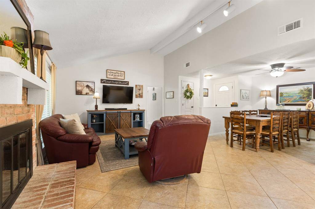 This inviting living and dining area features a cozy brick fireplace, tiled floors, and ample natural light, creating a warm and functional space.