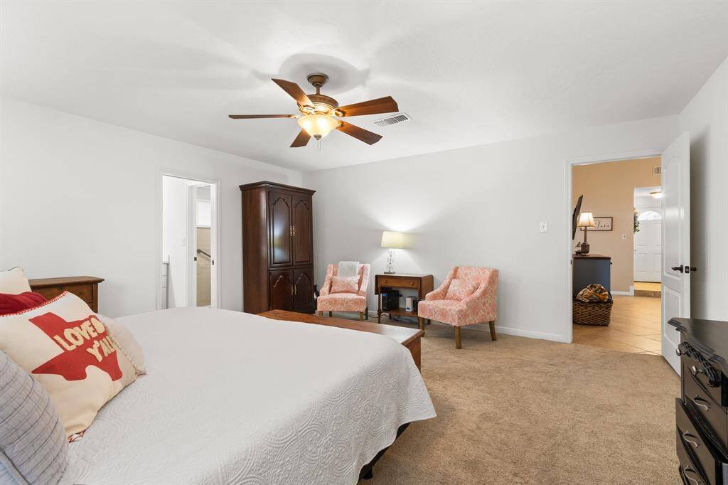 Spacious primary bedroom with neutral tones, featuring a ceiling fan, plush carpet, and ample natural light.  The room connects to an en-suite bathroom and has access to a hallway.
