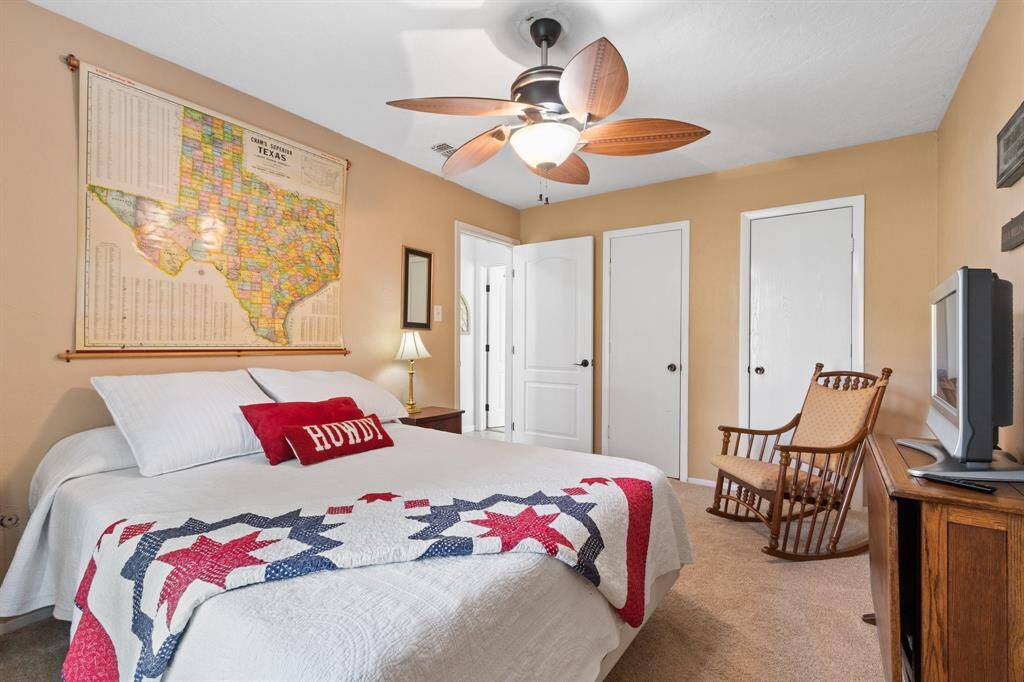 Cozy bedroom with warm, neutral walls and carpet. Features a ceiling fan and large connected closets.