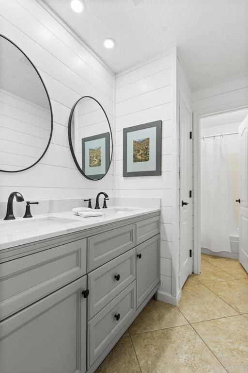 This secondary bathroom features a modern double vanity with round mirrors and sleek black fixtures. It has white shiplap walls and a neutral tile floor, creating a clean and contemporary look. Look behind the artwork on the side walls - they are medicine cabinets!