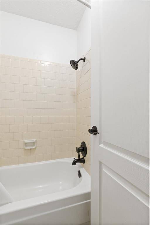 The secondary bathroom featuring a clean, white bathtub with beige tile walls. It includes a black showerhead and faucet, adding a modern touch.