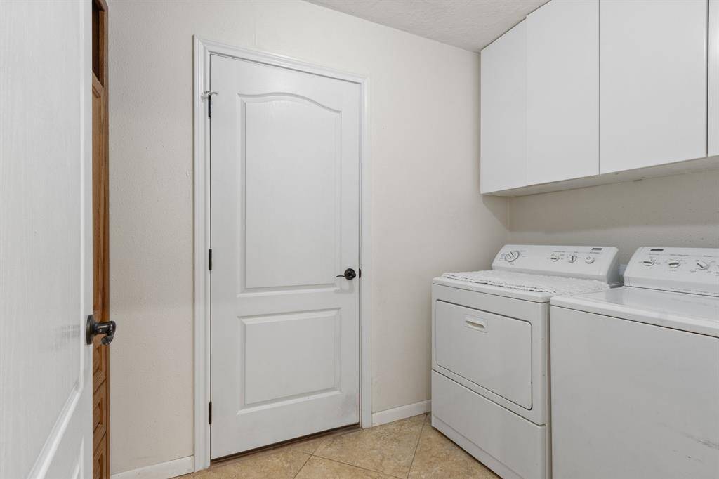 The laundry room with white cabinetry above for storage, and a neutral tile floor. The space is clean and functional, featuring a white door providing easy access.