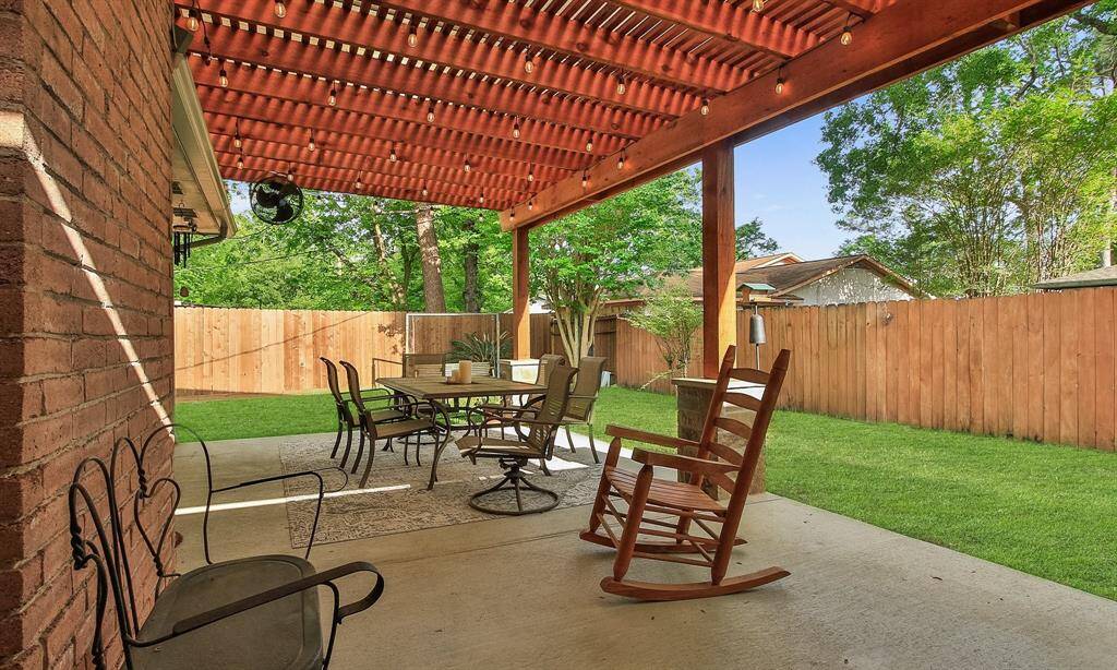 The backyard patio with a wooden pergola, providing a cozy outdoor seating area. The space is surrounded by a fenced-in yard with well-maintained grass and mature trees, offering a private and inviting atmosphere for relaxation or entertaining.