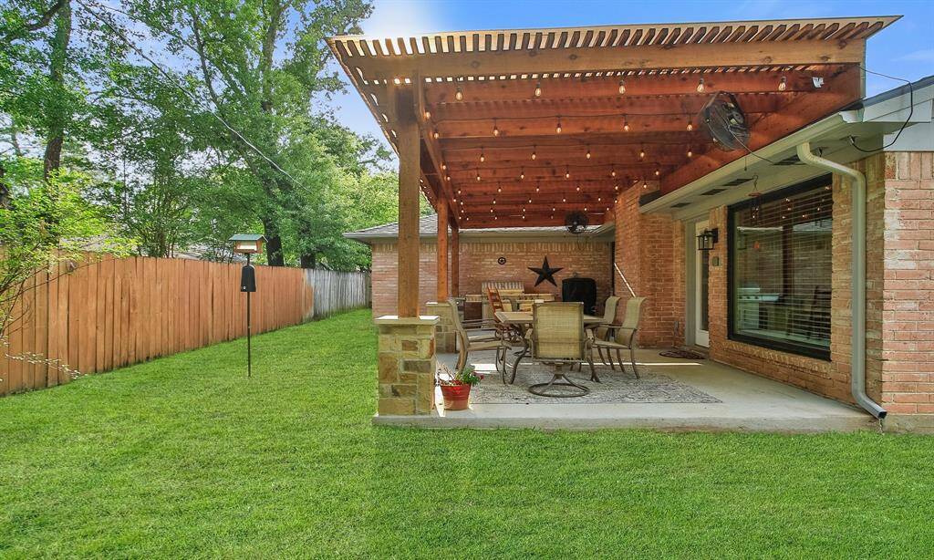 This inviting backyard features a spacious covered patio perfect for outdoor dining and entertaining. The area is surrounded by a neatly maintained lawn and enclosed by a wooden fence for privacy.