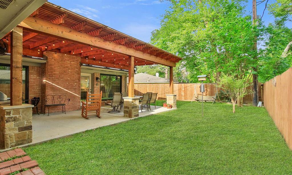 Such a charming backyard with a covered patio featuring wood details. It opens to a well-maintained lawn, enclosed by a wooden fence and shaded by mature trees, providing a cozy and private outdoor space.