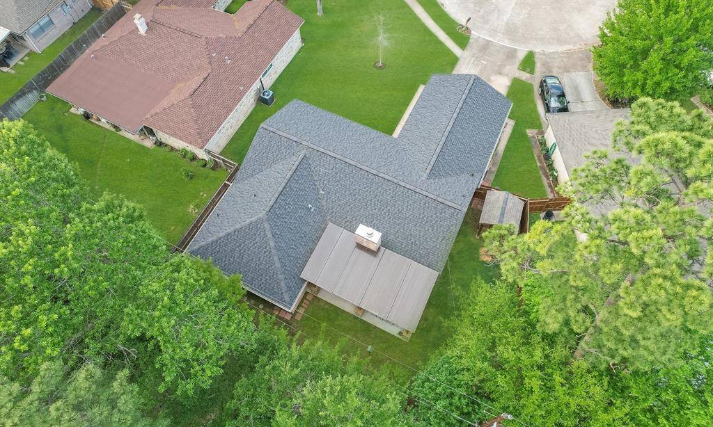 This aerial view showcases a single-story home with a recent roof replaced 2021, surrounded by a spacious, well-maintained green yard. It's located in a suburban setting with neighboring houses and a driveway leading to a cul-de-sac. The property is bordered by greenery, providing a sense of privacy.