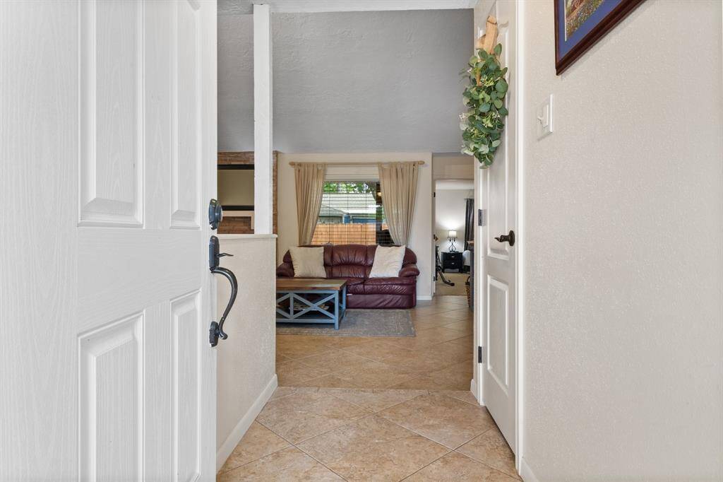 Welcome to a cozy living space with a warm tile floor and an inviting open layout. The room features large picture windows with blinds & curtains, perfect for family gatherings.