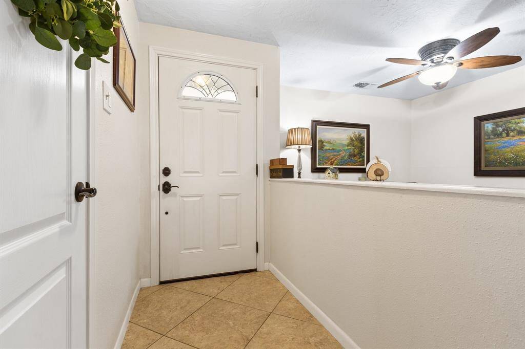 This inviting entryway features a tiled floor, a white door with decorative glass, and a ceiling fan with a light. The neutral walls create a welcoming atmosphere.