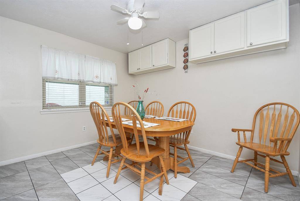 A bright, cozy dining area featuring tile floor, ample natural light from a window, and extra storage with white overhead cabinets.