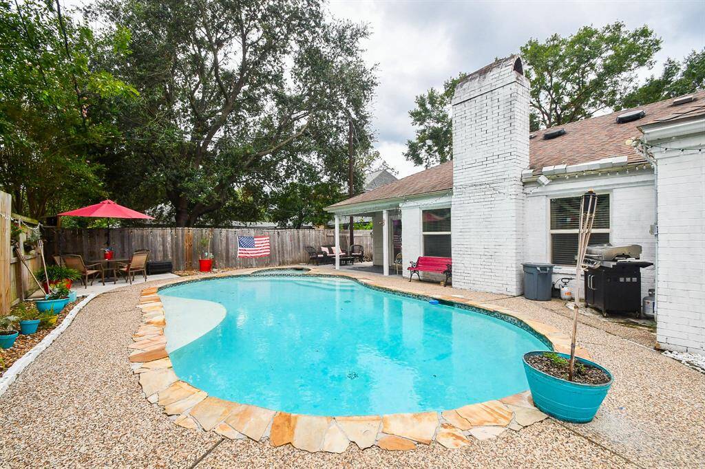 This photo showcases a cozy backyard with an inviting inground swimming pool, a patio area with seating under an umbrella, and a privacy fence. The home features a white-painted brick exterior. Perfect for outdoor entertainment and relaxation.