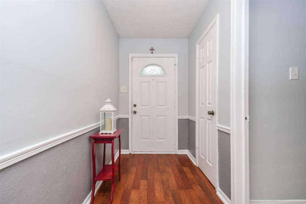 You're looking at a welcoming entryway featuring a white front door, complemented by neutral walls with chair rail accents and hardwood flooring. A small red table adds a pop of color to the space.