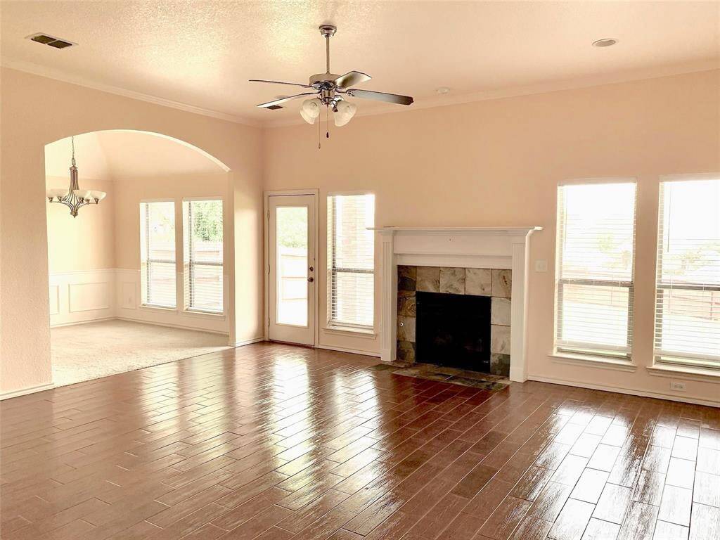 The spacious living room features high ceilings and well-placed windows that flood the space with natural light. A charming fireplace with a mantle serves as the centerpiece of the room, creating a warm & inviting atmosphere. Tile flooring and a neutral color palette offer versatile styling options.
