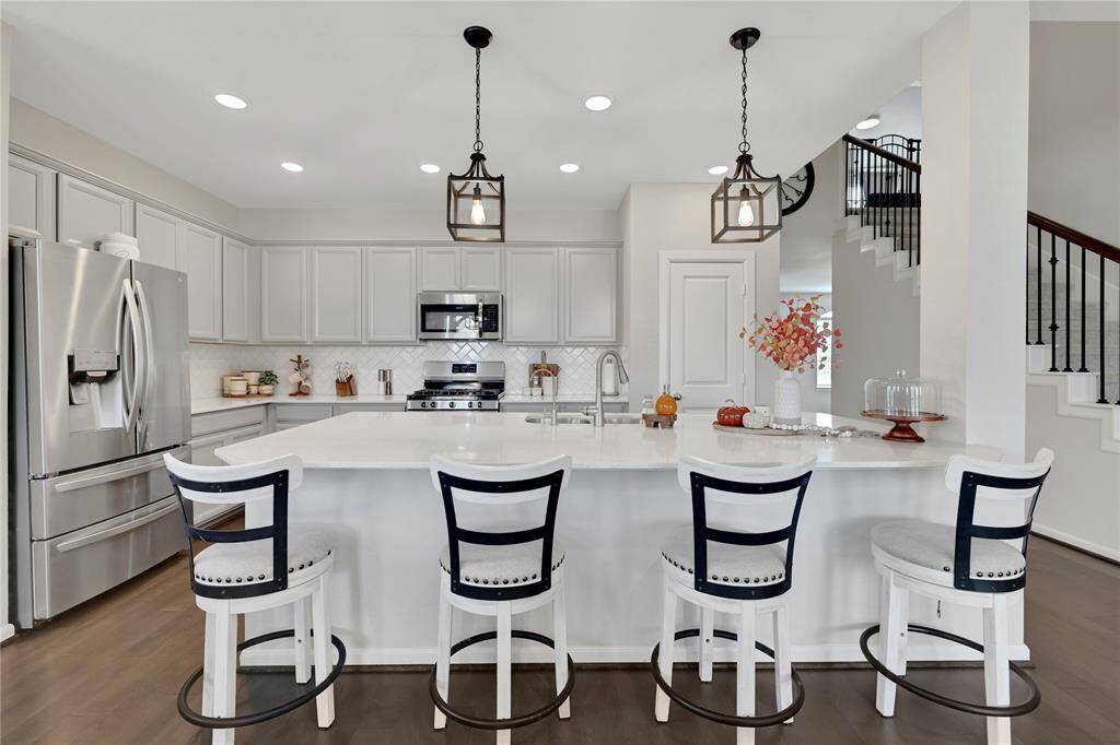 The modern open-concept kitchen with white cabinetry and stainless steel appliances. accents the island with seating, elegant pendant lights, and a view of the staircase leading to the upper level. The design is clean and contemporary.